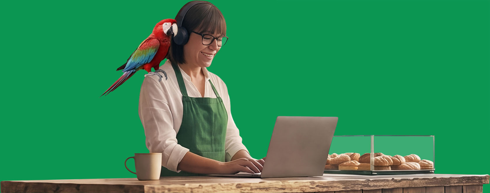 Café owner with a parrot on her shoulder working on a laptop at the counter